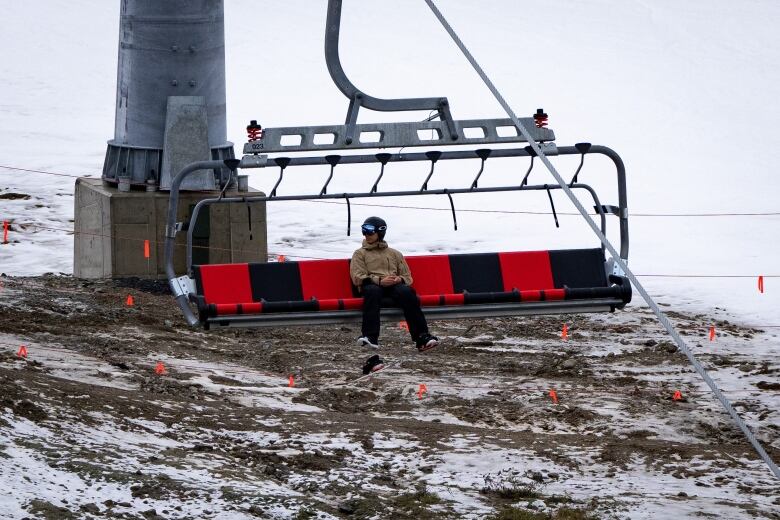 A skier on a ski lift with brown soil and dirt below him.