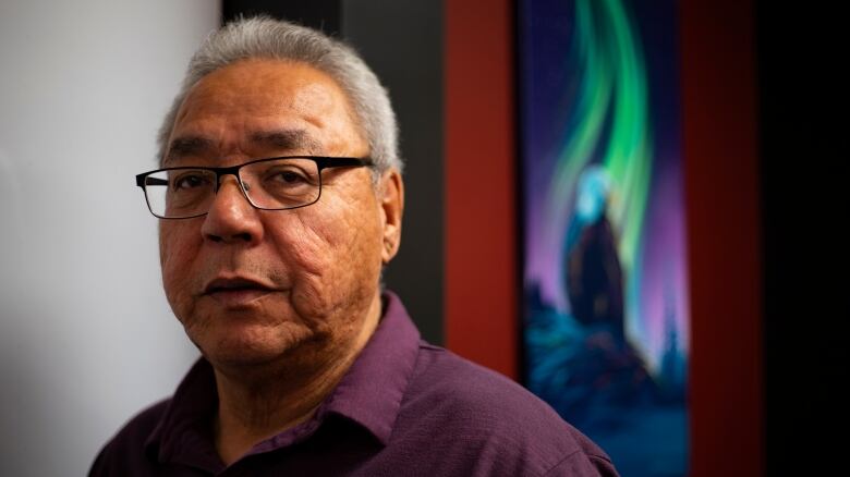 A man stands in front of a northern lights painting.