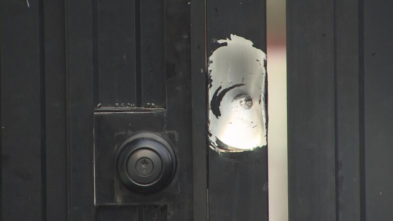 A metal gate with a black knob with a bullet hole next to it.