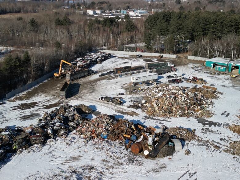 Heavy machinery loading large trucks with scrap metal near piles of snow-covered scrap.