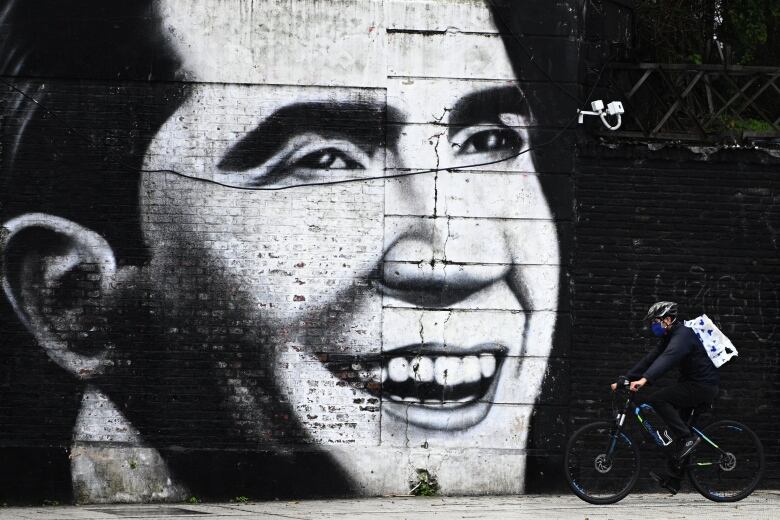 A man on bicycle passes a large mural showing the head of a smiling man.