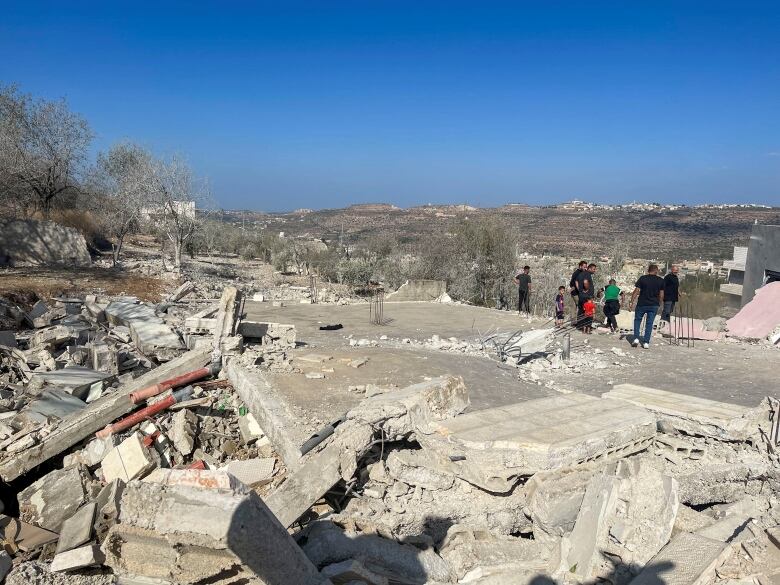 A group of people stand on top of concrete rubble where a house used to be.