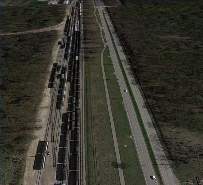 An aerial view of two forested areas separated by a four-lane roadway and train tracks.