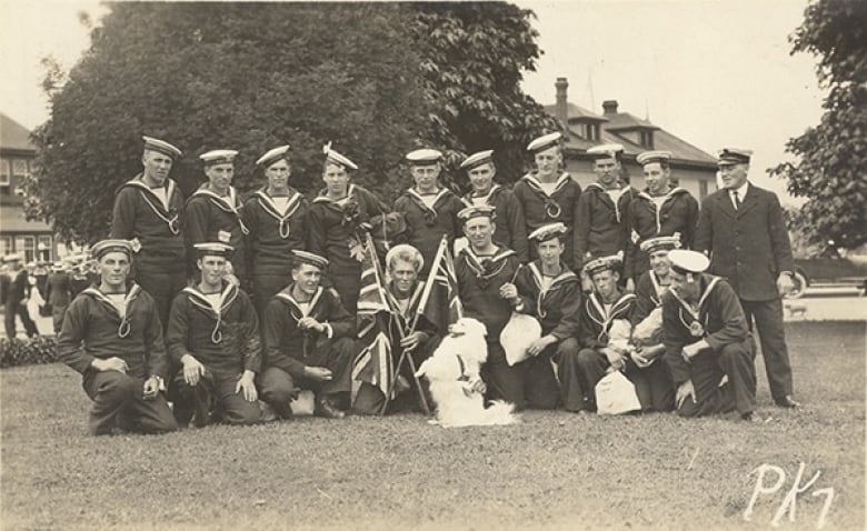 A group of naval officers sit around a white dog, carrying Union Jacks and smiling.