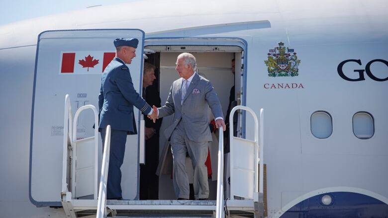 A white man shakes hands with another man in uniform while disembarking from a plane.