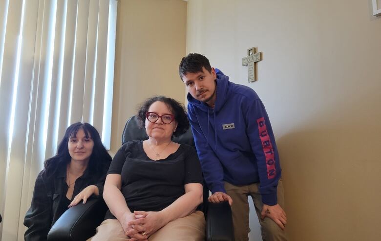 A woman sitting in a hospital-like chair with two younger people next to her.