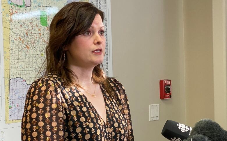 A woman in a patterned shirt speaks into a mic at a podium