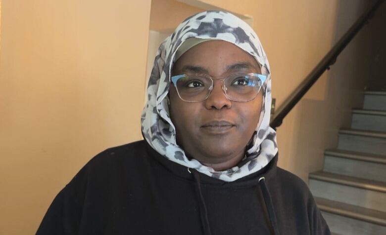 A woman wearing a hijab stands in her living room. 