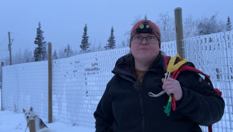 A woman wearing a headtorch and a toque with husky harnesses over her shoulder. 