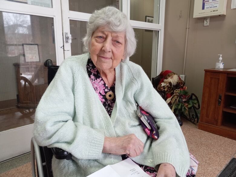 Older woman sitting in wheelchair holding a letter, wearing a light green sweater.