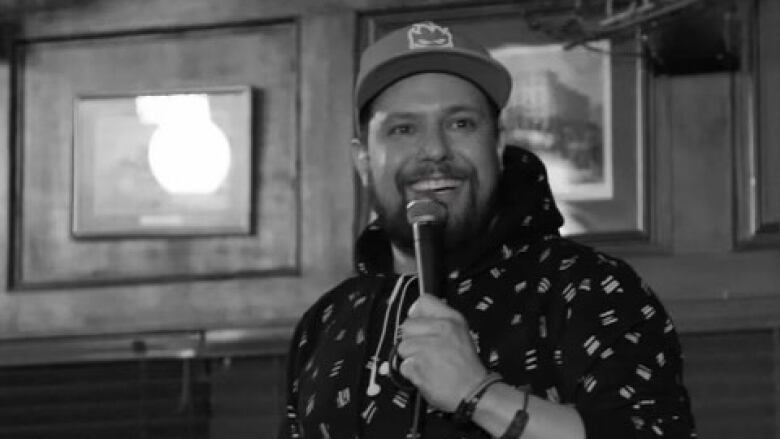 A black and white photo of a man holding an microphone in a stand up comedy setting