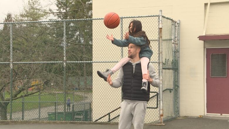 A man plays basketball with his daughter, who is up on his shoulders.