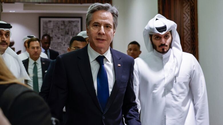 U.S. Secretary of State Antony Blinken walks with a man in a white headdress and robe