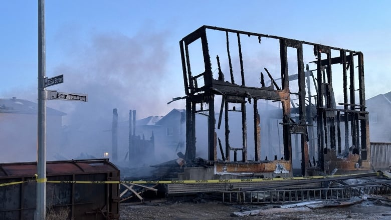 Smoke billows from the burned out structure of a home. The sun rises in the background.