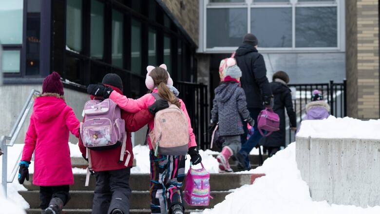 Children in winter coats walk up to school entrance.