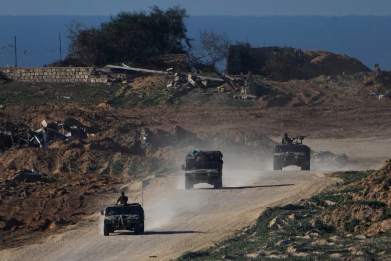 Three tanks move in a line along a dirt road. 