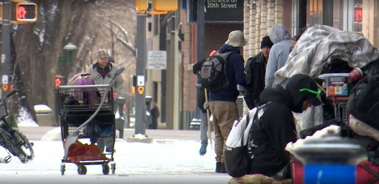 A group of people huddle on the sidewalk in the winter snow 