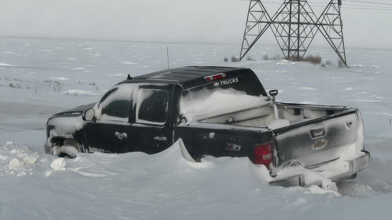 A black truck stranded in snow during a winter storm.