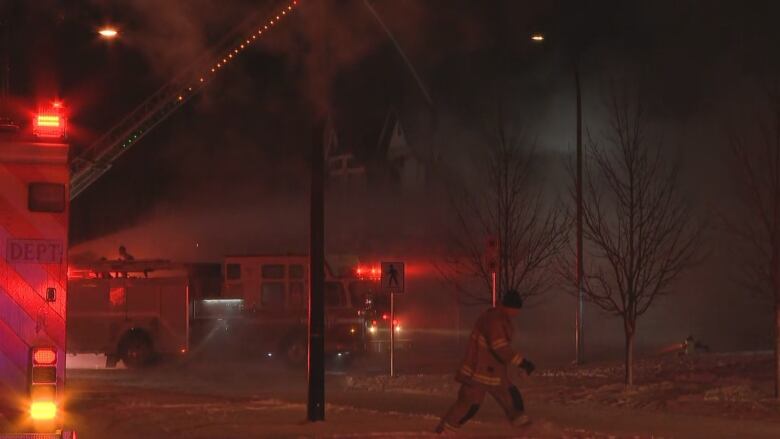 A firefighter walks past a burning house while a fire truck sprays in with water.