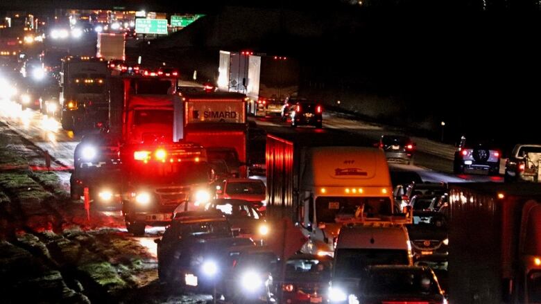 Lines of traffic and cars on the shoulder can be seen on a highway at night.