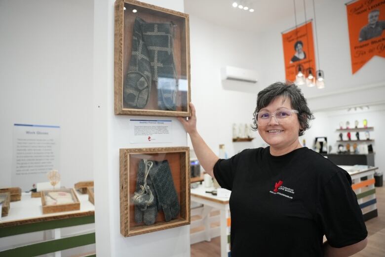 Woman with short hair wearing a black shirt standing in front of gloves inside a picture frame.