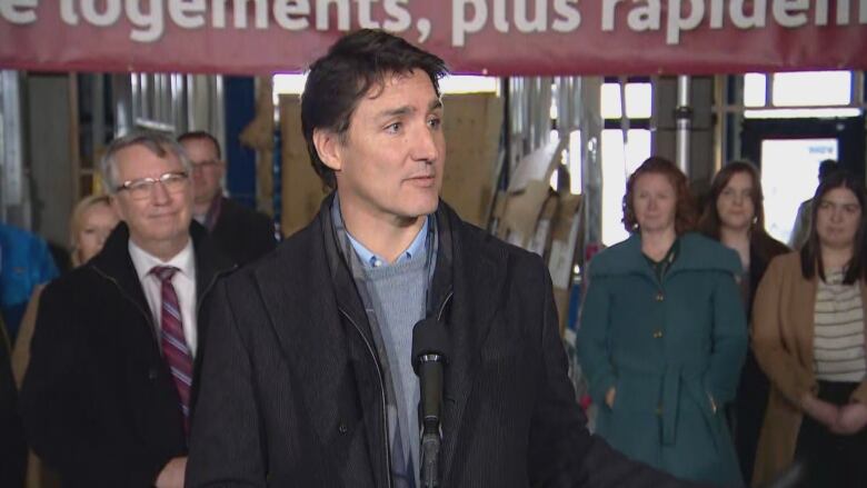 Man at microphone with people gathered behind him during a press conference