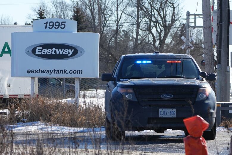 A police vehicle next to a sign for Eastway Tank in winter.