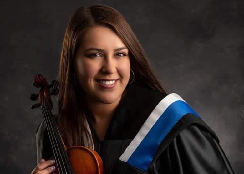 A woman in graduation robes holds a violin. 