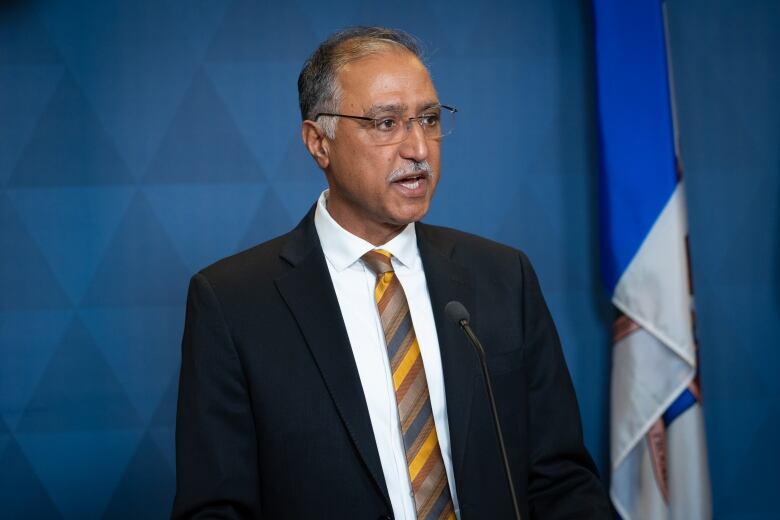 A man stands at a podium with a blue background. 