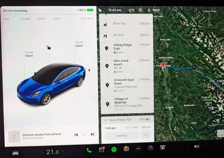 Photo of a navigation screen in the tesla. On the right is a map with a higlight route and red arrow. On the left is an animated image of a blue Tesla. In the middle is a panel highlighting a route with battery percentages from Prince George to McBride. 