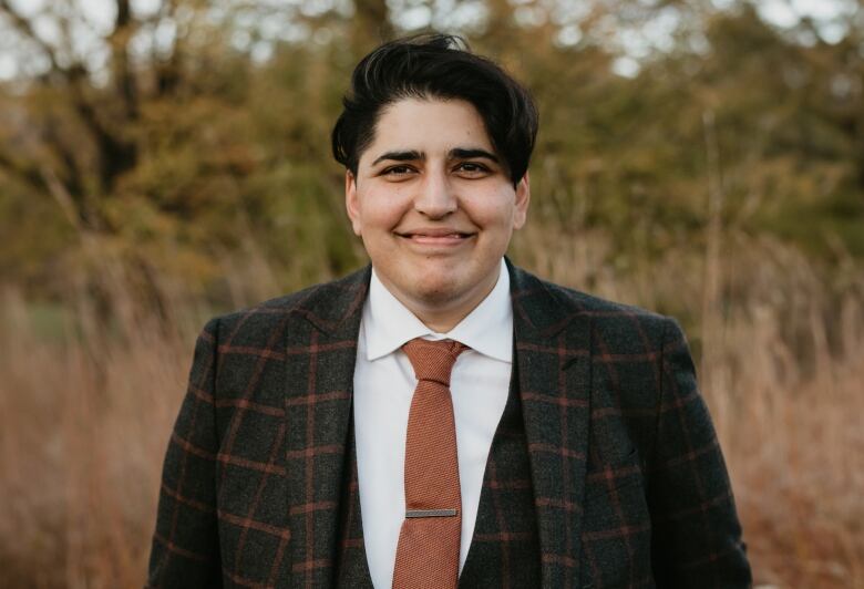 A person in a burnt orange tie and plaid jacket is pictured outdoors