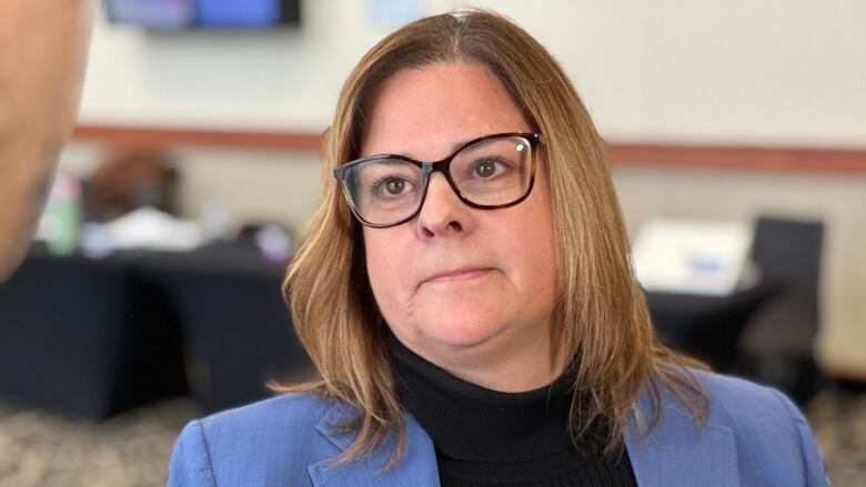 A woman in a blue blazer and black sweater looks upward.