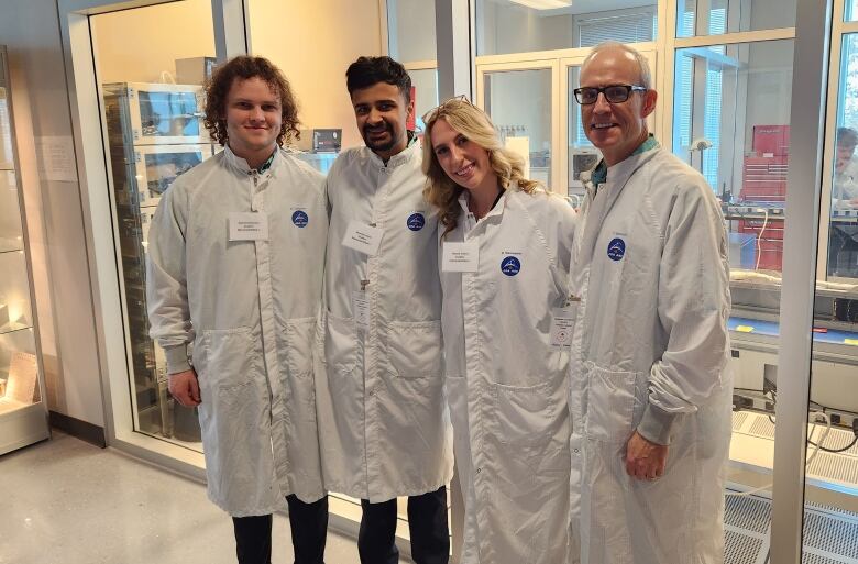 Four people wearing white coats stand in a laboratory. 