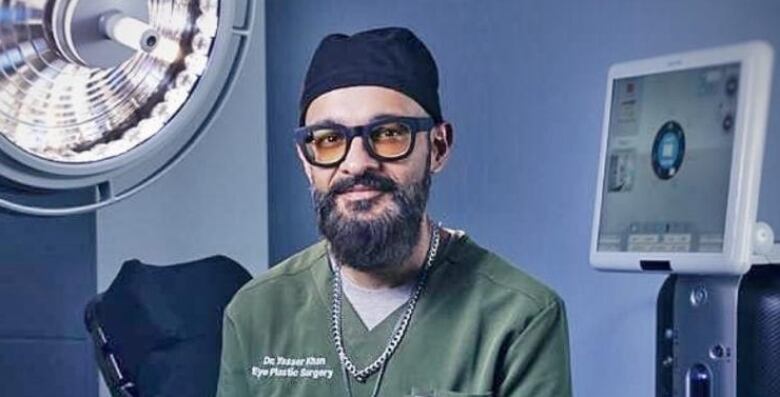 A man wearing medical scrubs sits in an operating studio in a posed portrait.