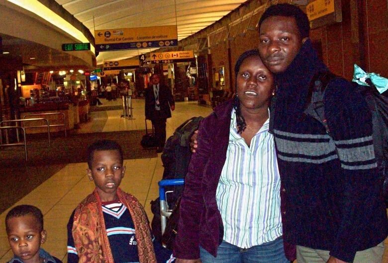 A Nigerian family is seen standing at an airport in this photo that includes two little boys, a man, and a woman with bags and a suitcase.