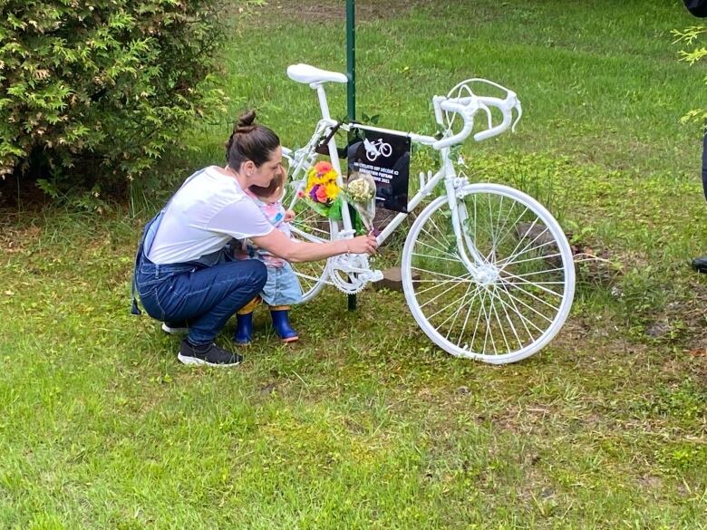 A woman places flowers on a white bicycle. A small child is with her. 