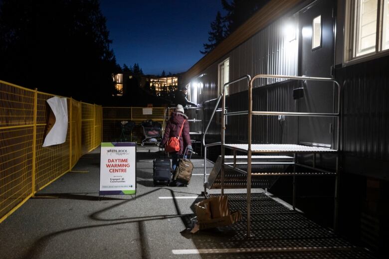 A woman pulls two suitcases behind her as she walks toward a portable trailer.