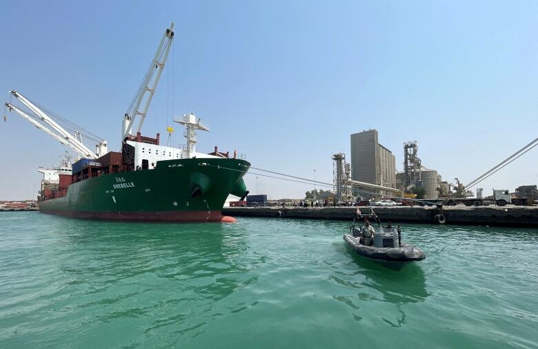 A cargo ship in port with a rubber inflatable boat near it.