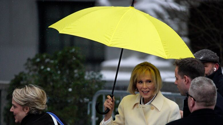 A woman in a coat holds up an umbrella in an outdoor photograph.