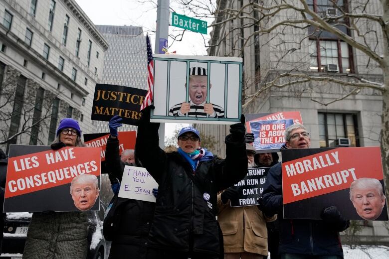 Several people carry signs at a demonstration outside. The signs read 'Justice Matters,' 'Lies have Consequences,' and 'Morally Bankrupt.'