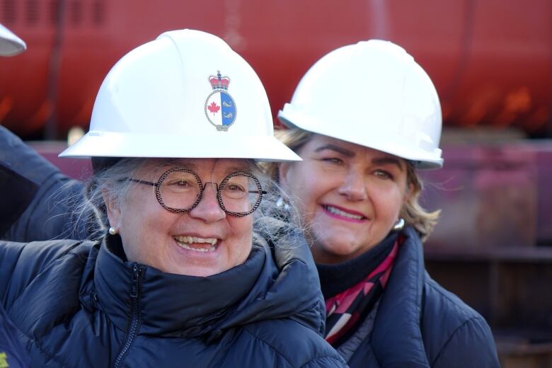 Two woman in white hard hats smiling.