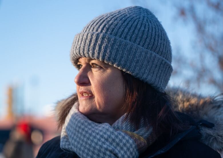 A closeup of a woman wearing a knitted tuque and a scarf speaking outside.