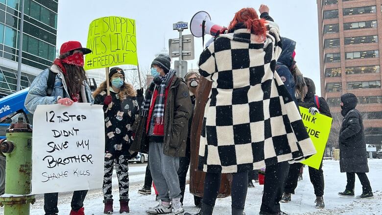 People stand in downtown Calgary with signs and a megaphone during a rally