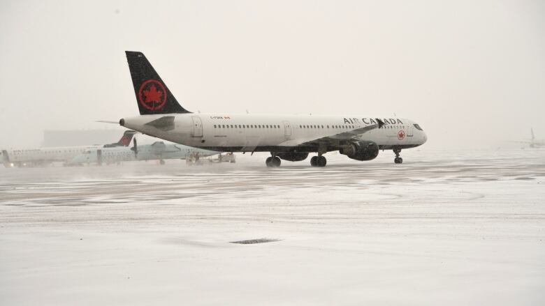 An Air Canada airplane on a tarmac as snow blows around it.