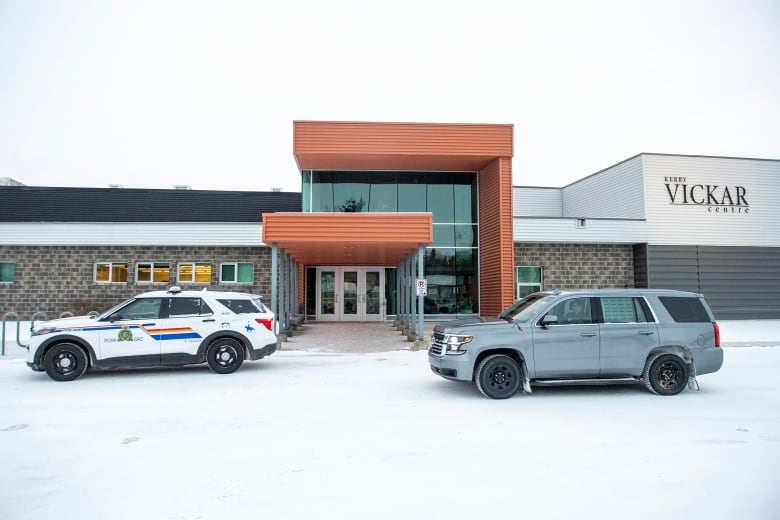 a police cruise and SUV are parked outside of a large building