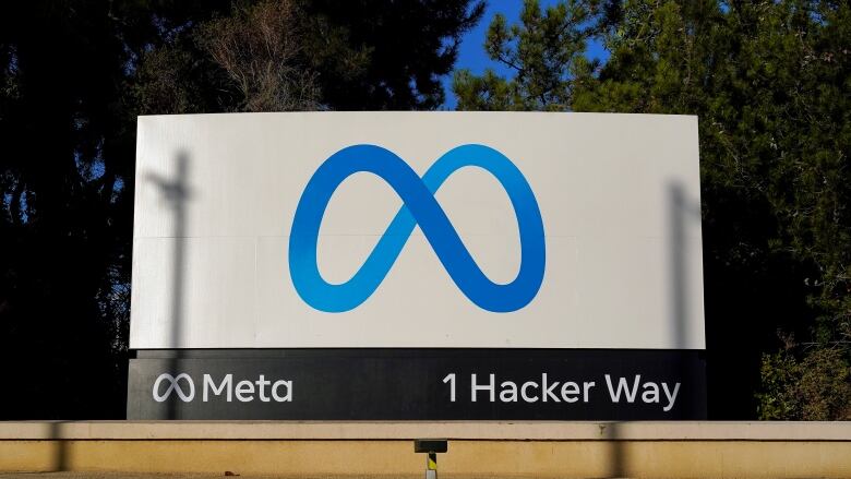 A large white sign with a blue infinity symbol in front of green trees in the background. 