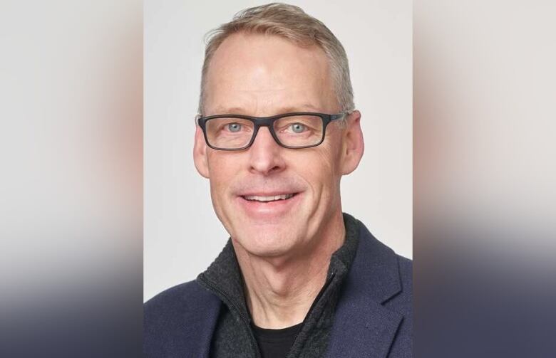 A smiling man with grey hair and dark-rimmed glasses 