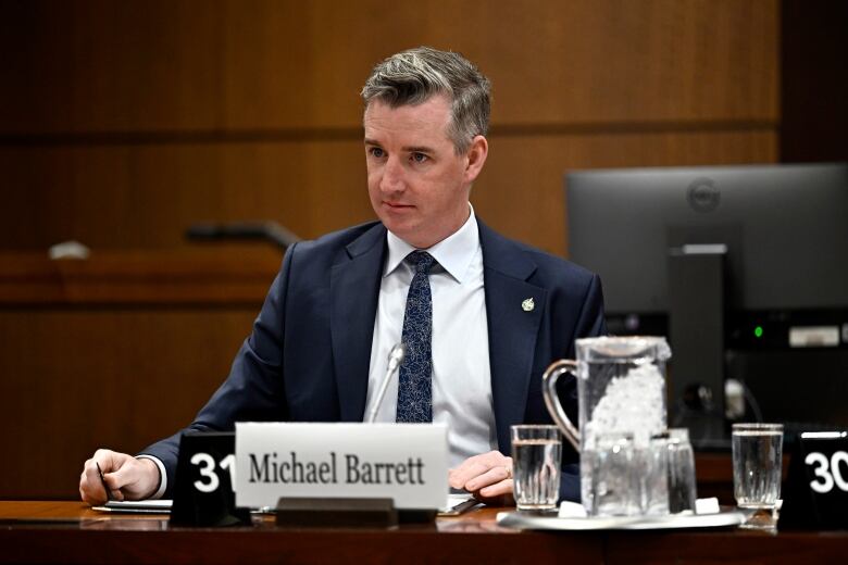 A politician sits at a desk with a microphone before the start of a meeting.