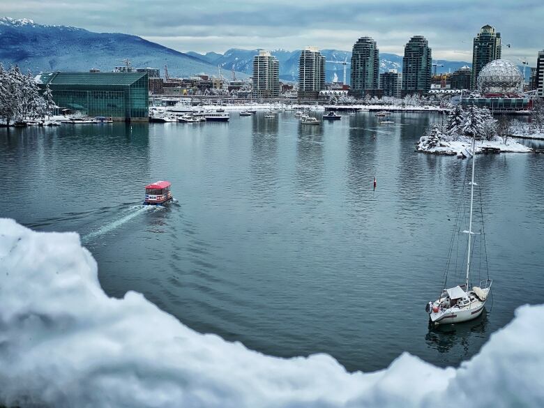 Two boats appear in False Creek with snow in the foreground and snowy mountains in the background.