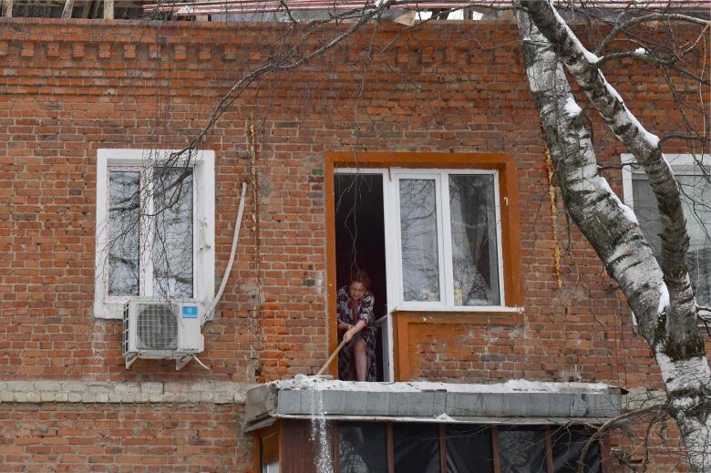 A woman clears snow off the balcony of a damaged building in Belgorod, Russia.